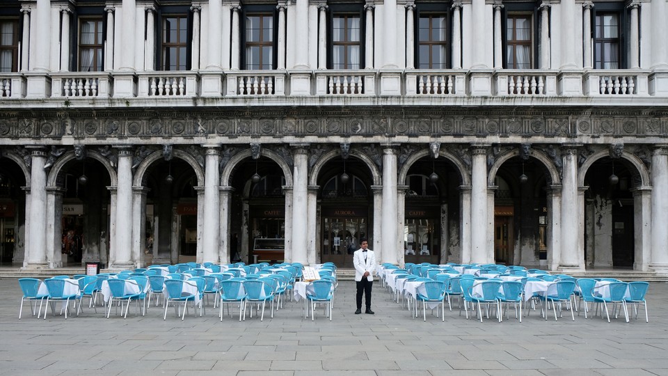 A waiter stands by empty tables outside a restaurant at St Mark's Square, which is usually full of tourists, after Italy's government adopted a decree with new emergency measures to contain the coronavirus