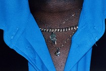 A close-up of an upper chest with a bright-blue shirt and three necklaces, including a gold chain and half a heart