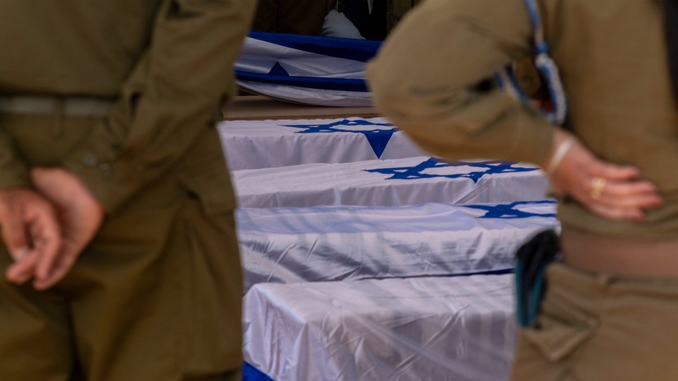 Soldiers looking solemnly at graves covered in Israeli flags