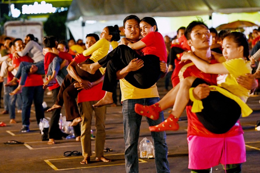Dozens of men stand carrying women in a parking lot.