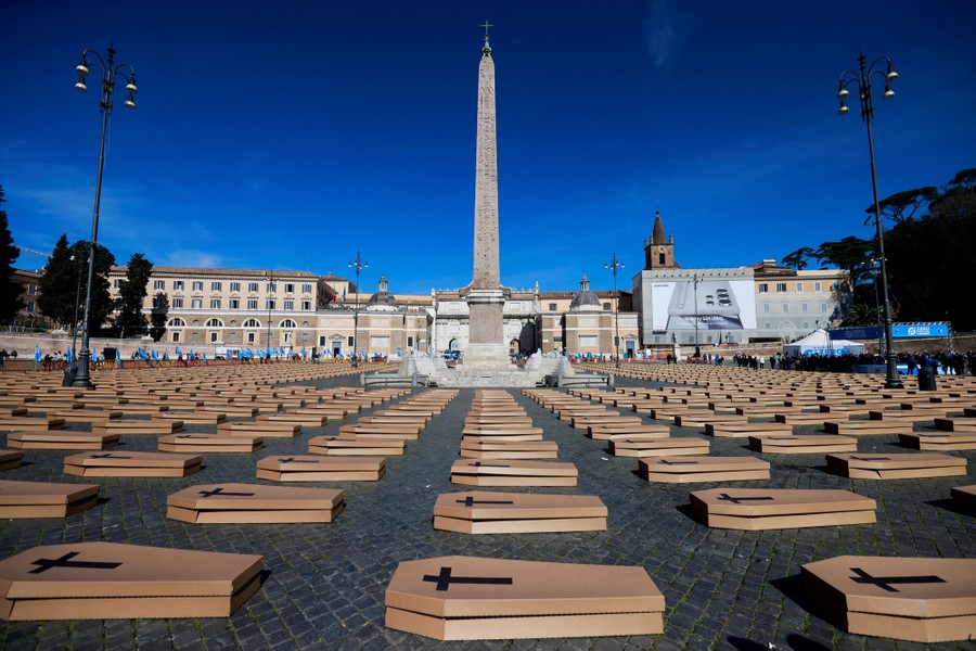 Hundreds of cardboard coffins are arranged in rows in a city square.