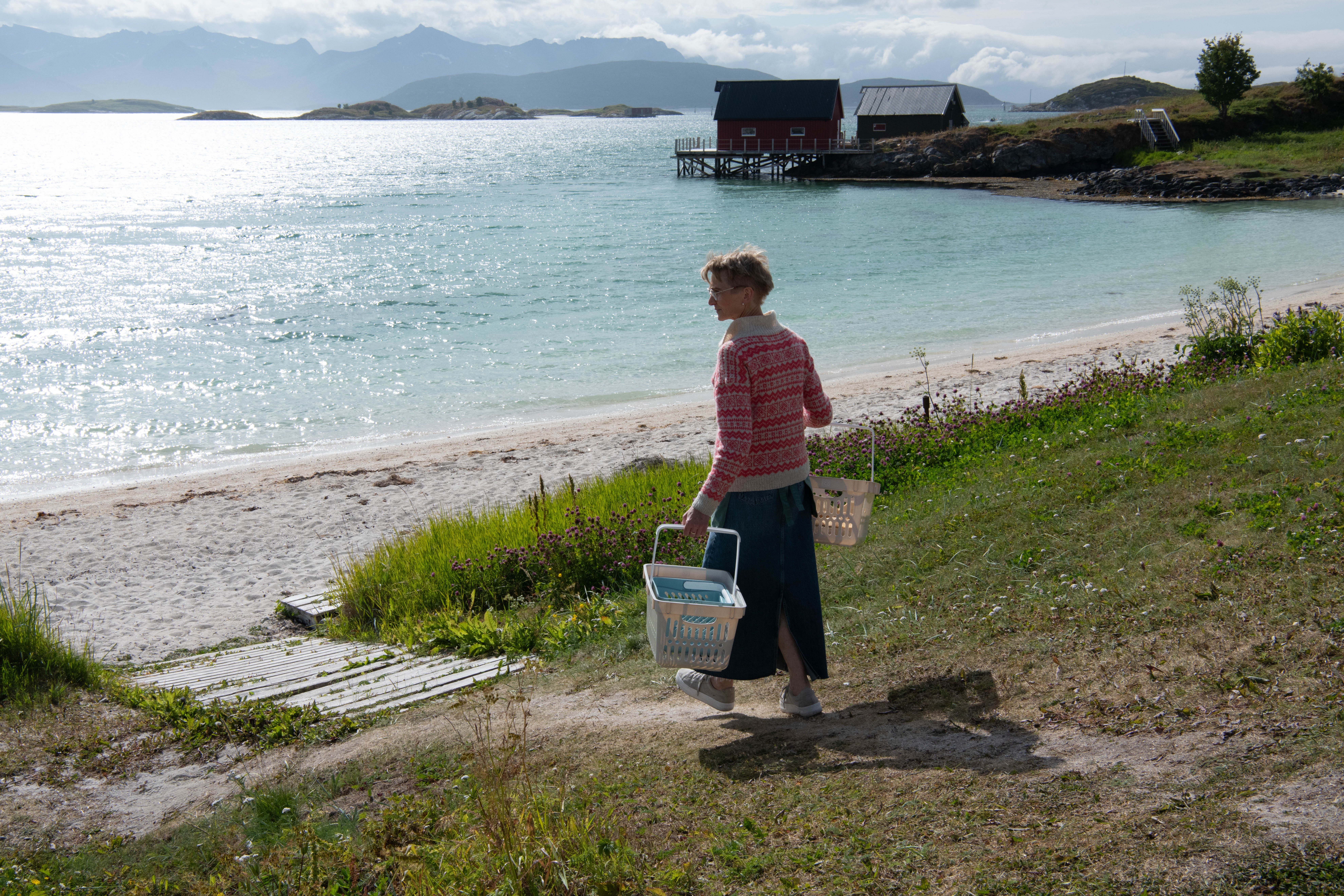 A color photograph of a woman carrying large baskets while walking to the beach