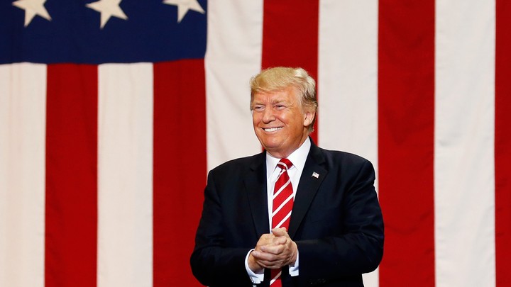 Donald Trump smiles in front of an American flag.