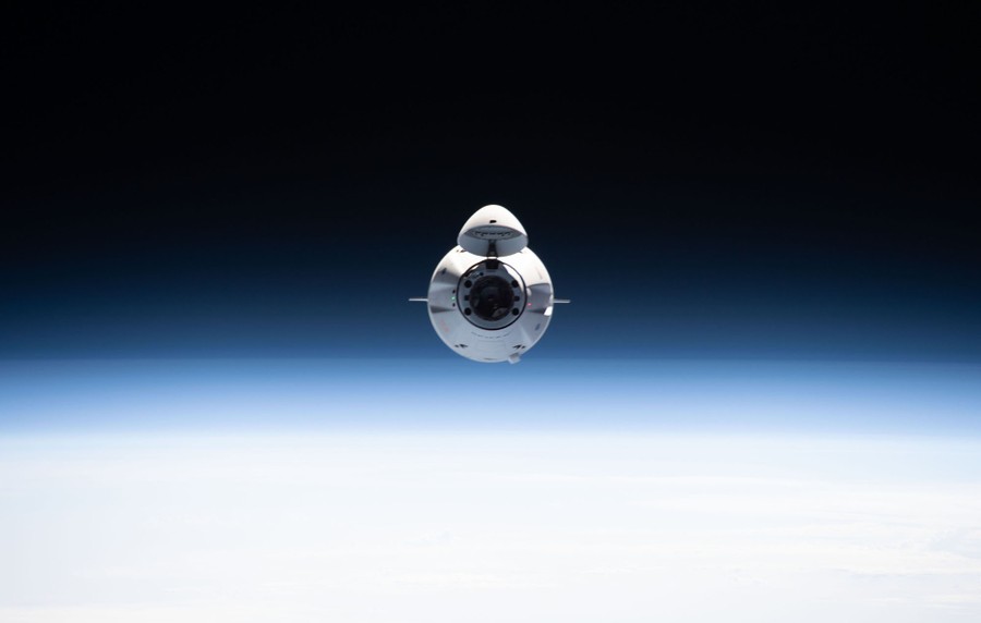 A small white spacecraft is seen just above the horizon, heading toward the photographer.