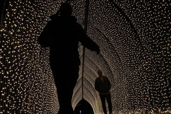 People walk through a tunnel of lights at Kew's Christmas light trail at the Royal Botanic Gardens in Kew, London, on November 15, 2022.