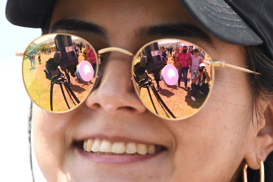 An image of the annular solar eclipse seen through a telescope is reflected in the sunglasses of a young woman.