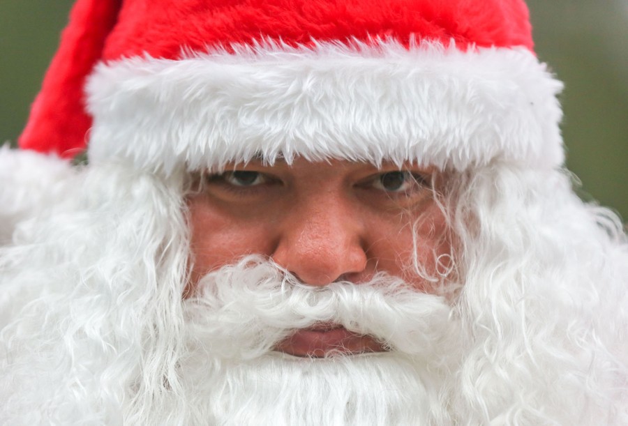 A close portrait of a person wearing a Santa Claus hat, wig, and beard
