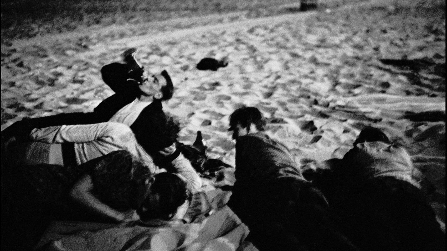 A group of young people lying on the beach, drinking in the sand at night