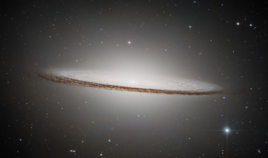 A disc-shaped galaxy, seen edge-on, ringed by clouds of darker dust