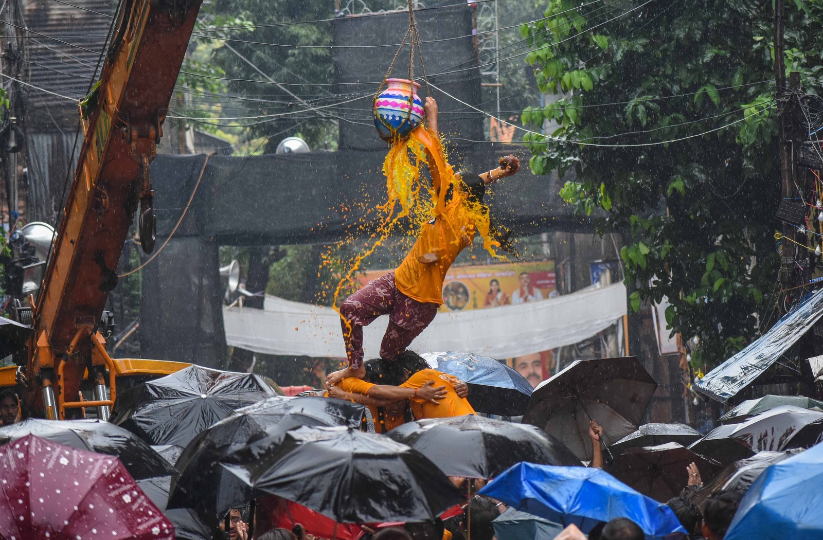 People form a small human pyramid to break a suspended pot during a festival on a rainy day in India.