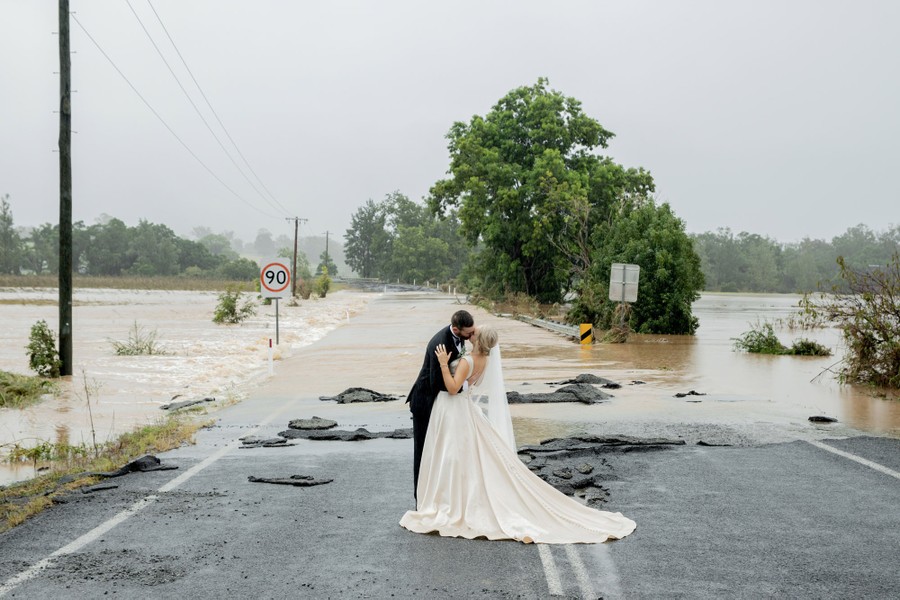 A bride and groom, dressed for their wedding, kiss while standing on a flooded road.