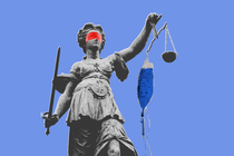 A sculpture of Lady Justice wearing a red blindfold and holding a bag of blue IV medicine