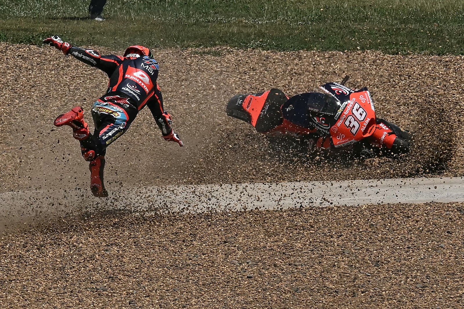 A motorcycle racer tumbles after a crash, appearing as if they were running toward their motorcycle sliding across gravel.