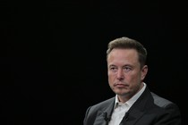 Elon Musk sits in front of a black background