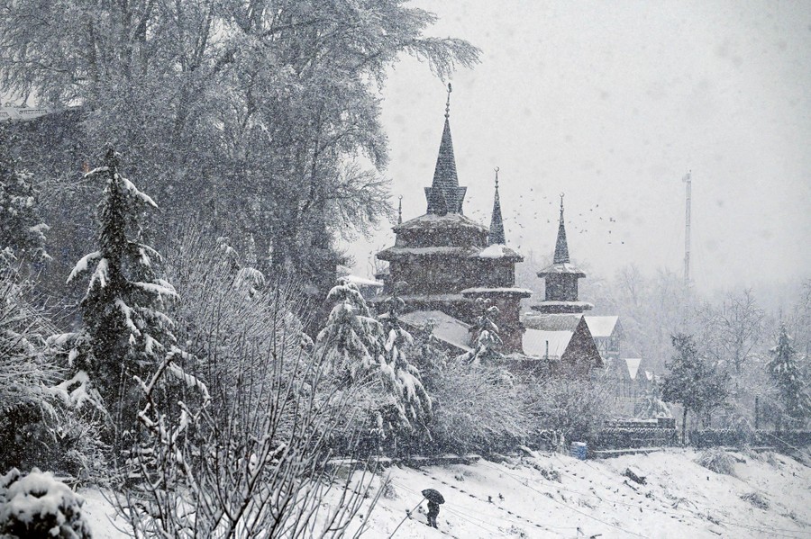 Snow falls on trees and a spired building.