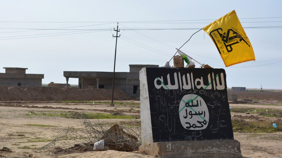 A flag of the Shiite militant group Saraya al-Khorasani flutters over a mural depicting the emblem of the Islamic State in Al-Alam, a village in Iraq.