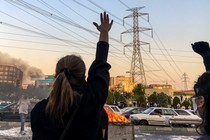 Women raise their hands in protest in front of a burning dumpster during the 2022 demonstrations in Tehran