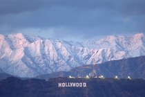 A distant view of the famous "Hollywood" sign, with snow-covered mountains in the background.
