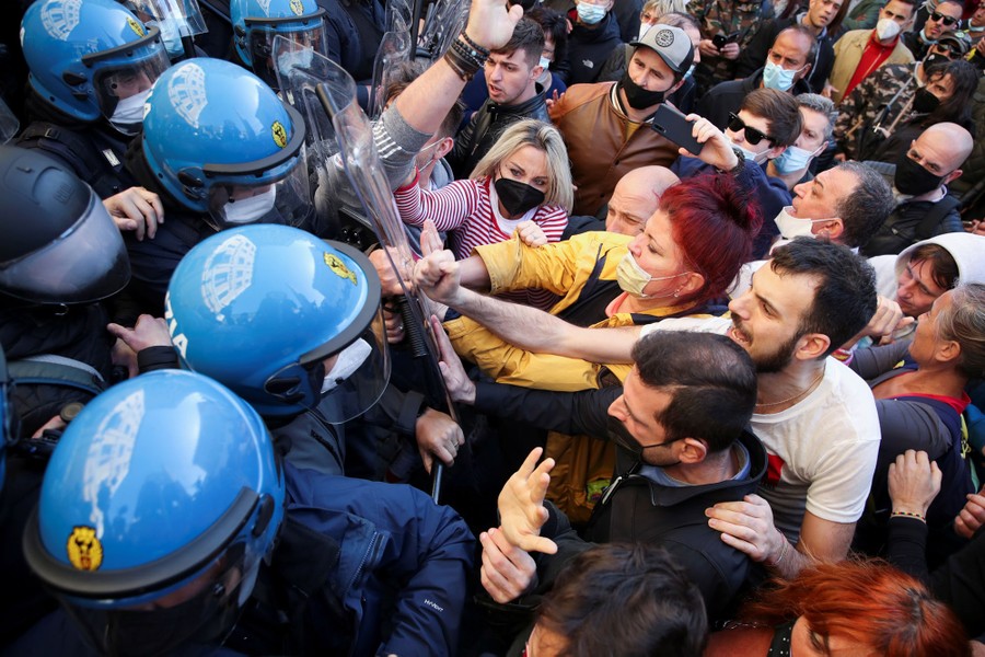 A crowd of people push against a group of riot-police officers.