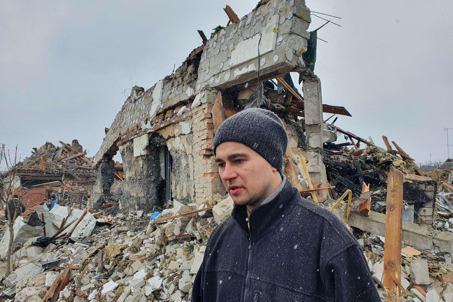 A man stands in front of rubble of several destroyed buildings.