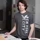 A boy wearing a gray shirt stands near a counter.