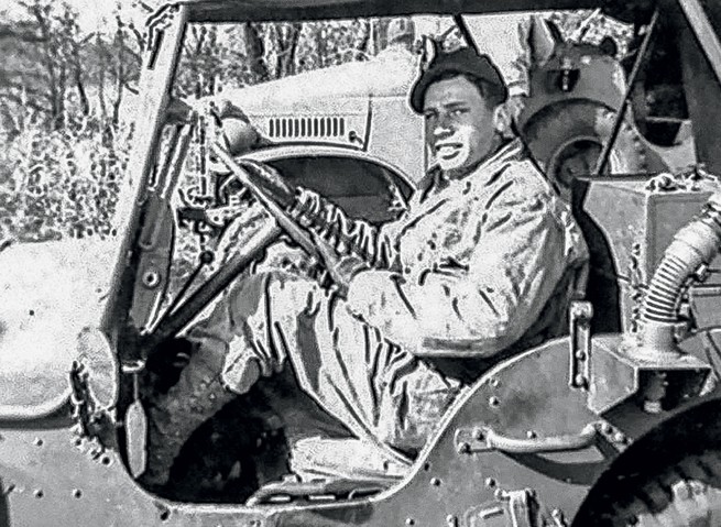 black-and-white photo of smiling uniformed soldier at the wheel of a Jeep