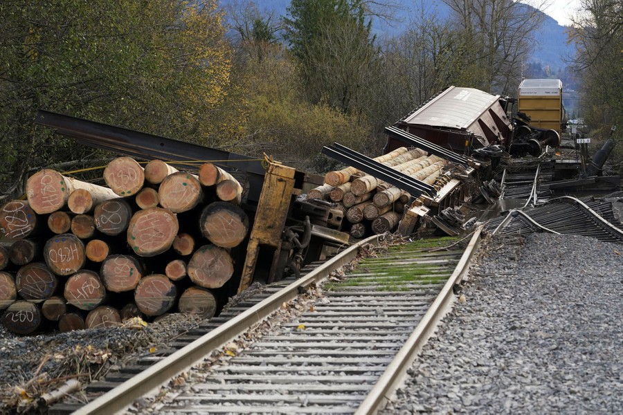 Several freight rail cars lie on  their sides along a heavily-damaged railroad track.