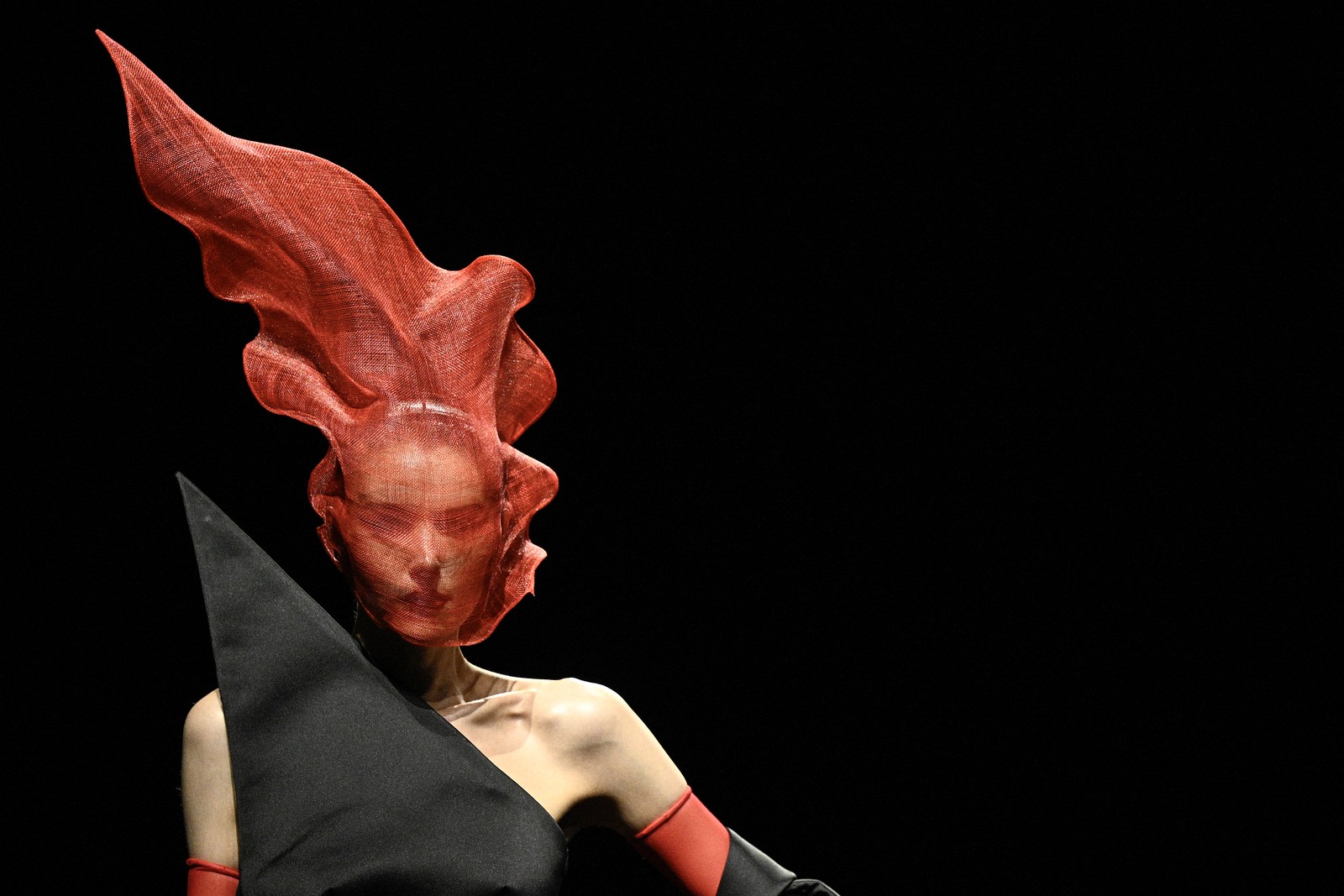 A model poses, wearing a garment that includes a tall flame-like headpiece.