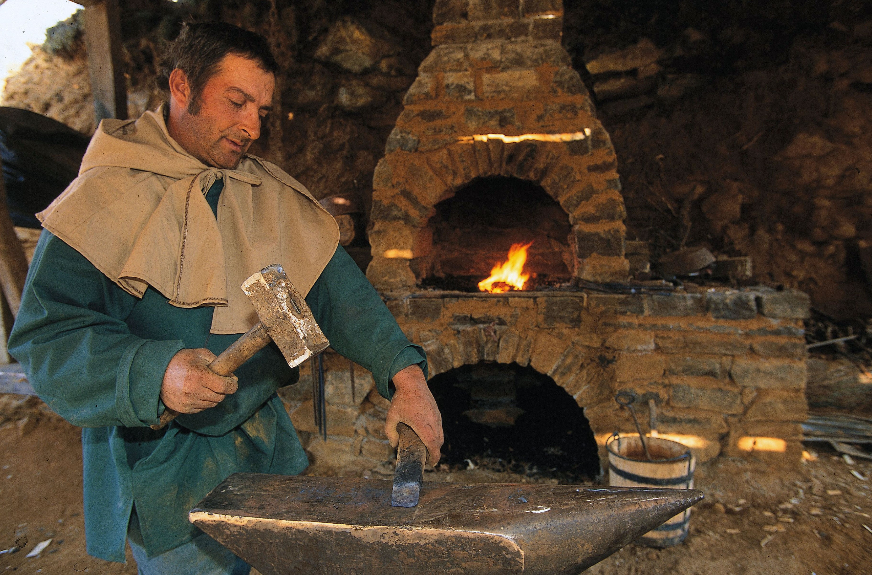 A blacksmith in medieval attire works at an anvil.