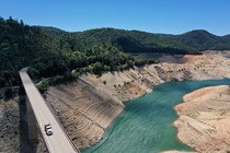A truck drives over a bridge that spans a reservoir, which is filled with water at a very low level.