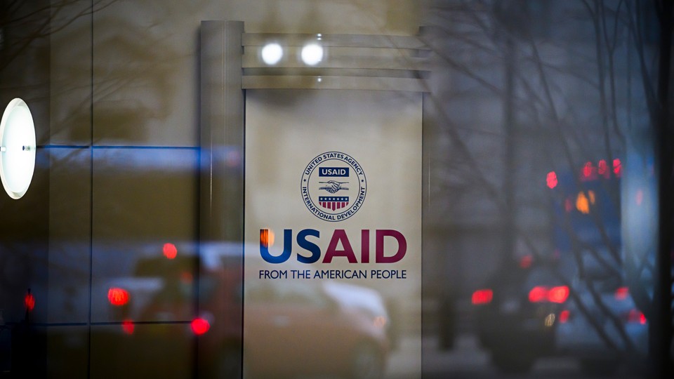 A sign for USAID with traffic reflected in a window