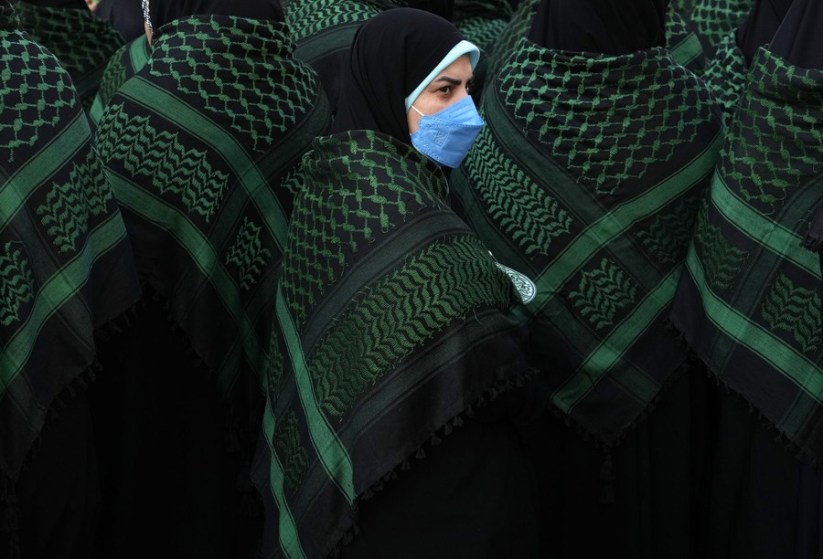 A group of women in long black–and-green garments attend a parade.