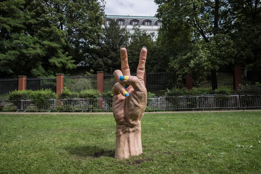 A giant sculpture of a hand giving a victory sign stands in grass outside a Russian embassy. Its fingernails are painted yellow and blue.