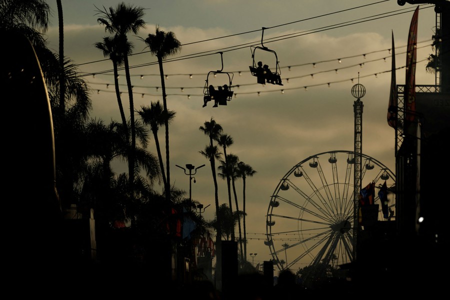 People ride in a chairlift-like "sky ride" past palm trees, with a Ferris wheel in the background.