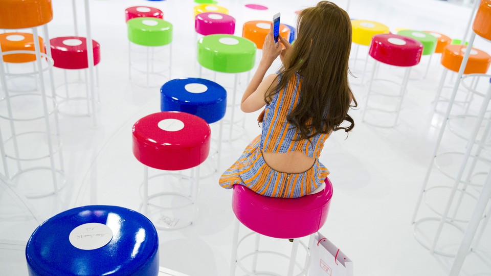 A woman looks at her phone while sitting among colorful stools.