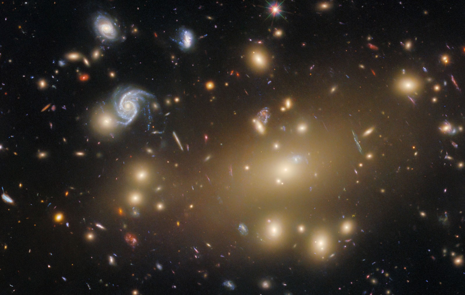 About a hundred galaxies of varying shapes and sizes, some of them appearing stretched and warped