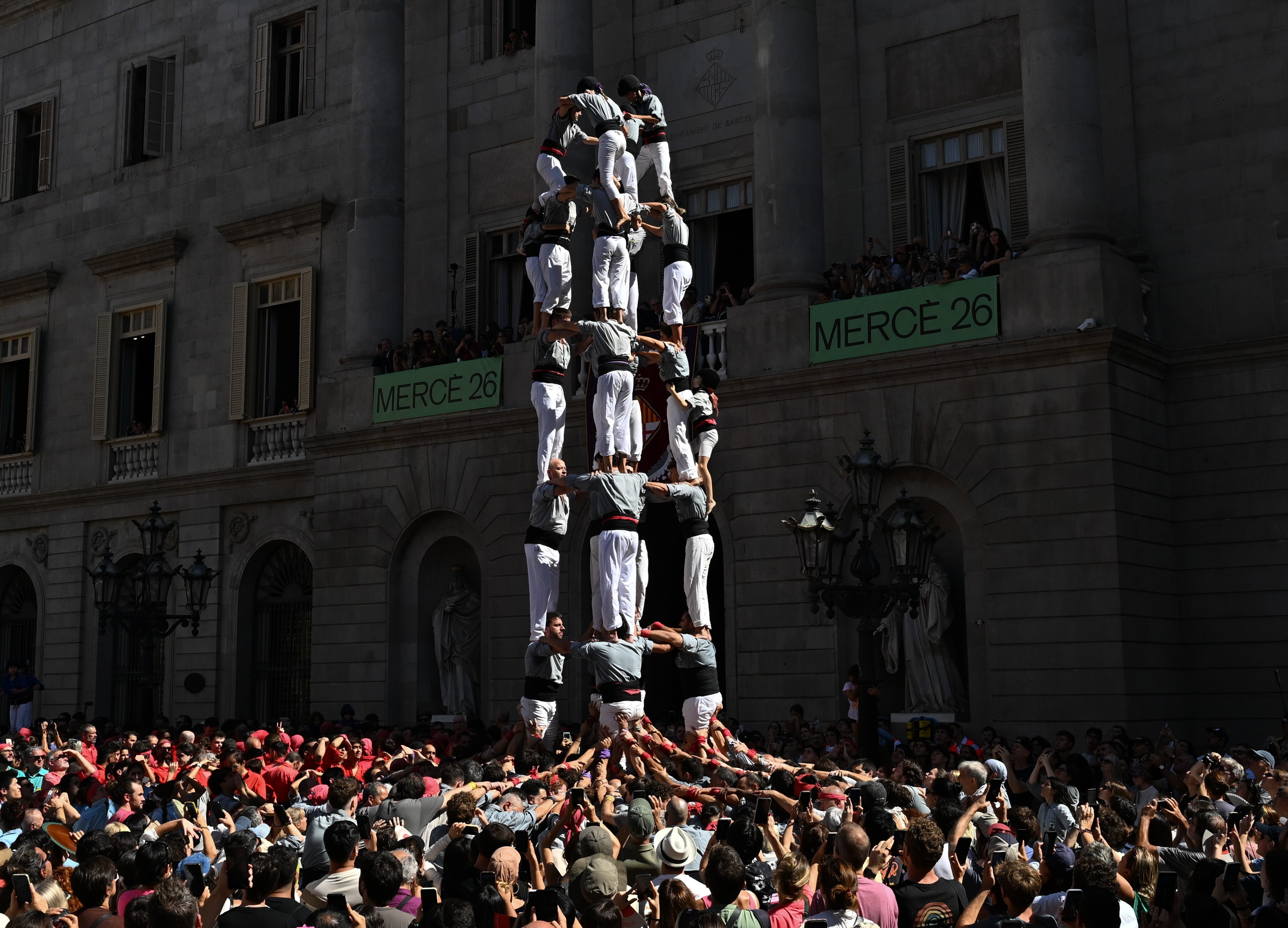 People watch as a human tower is formed, about six people tall.