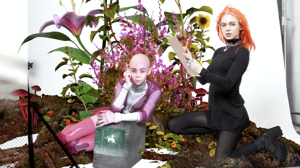 Grimes, in an orange wig, sits amid a field of flowers.