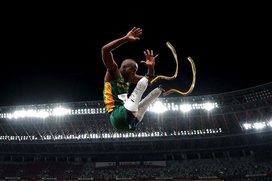 An athlete with two prosthetic legs leaps in a long jump.