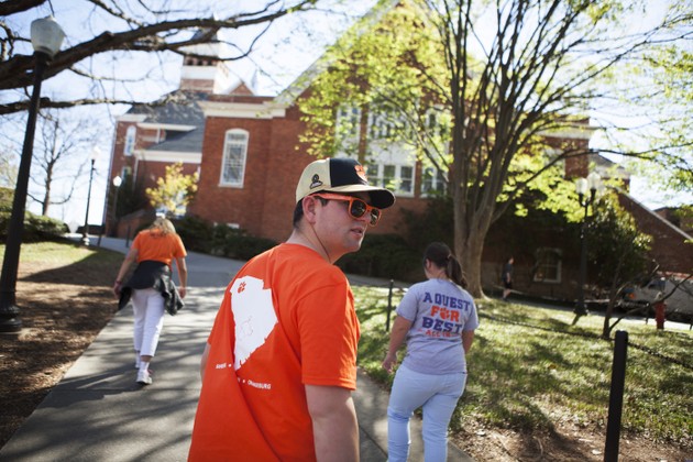 Students walk in front of a stately brick building. All three are wearing Clemson apparel