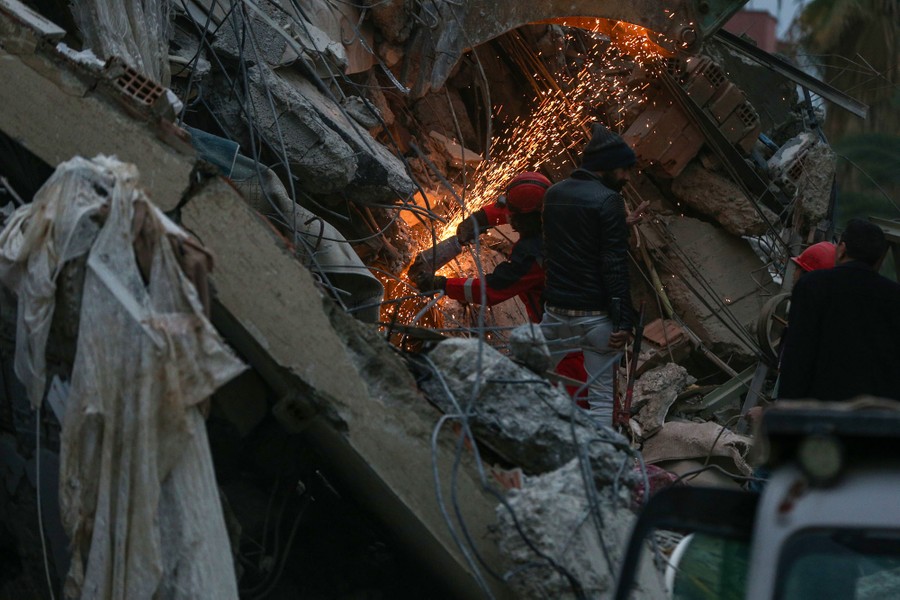 A rescue worker uses a power tool to cut through steel rebar in the rubble of a collapsed building.