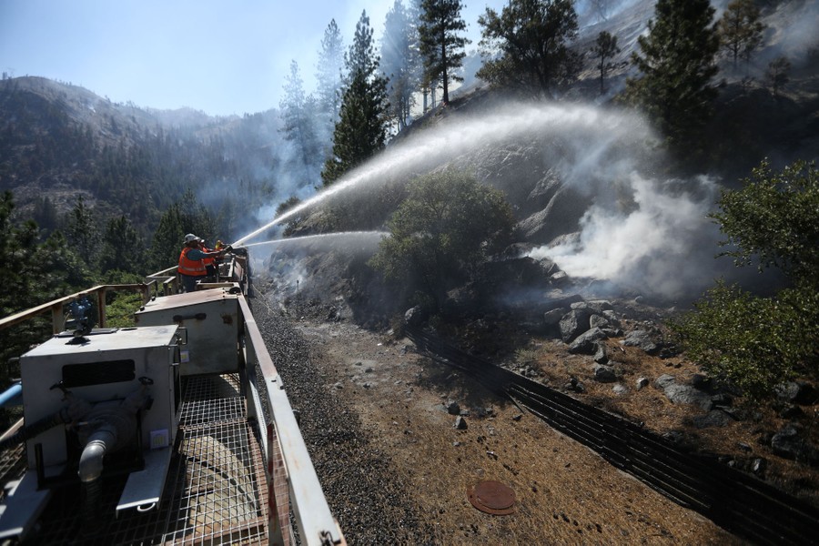 Firefighters spray water at smoldering brush from a fire train.
