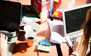 Two people work at laptops on a cluttered table.
