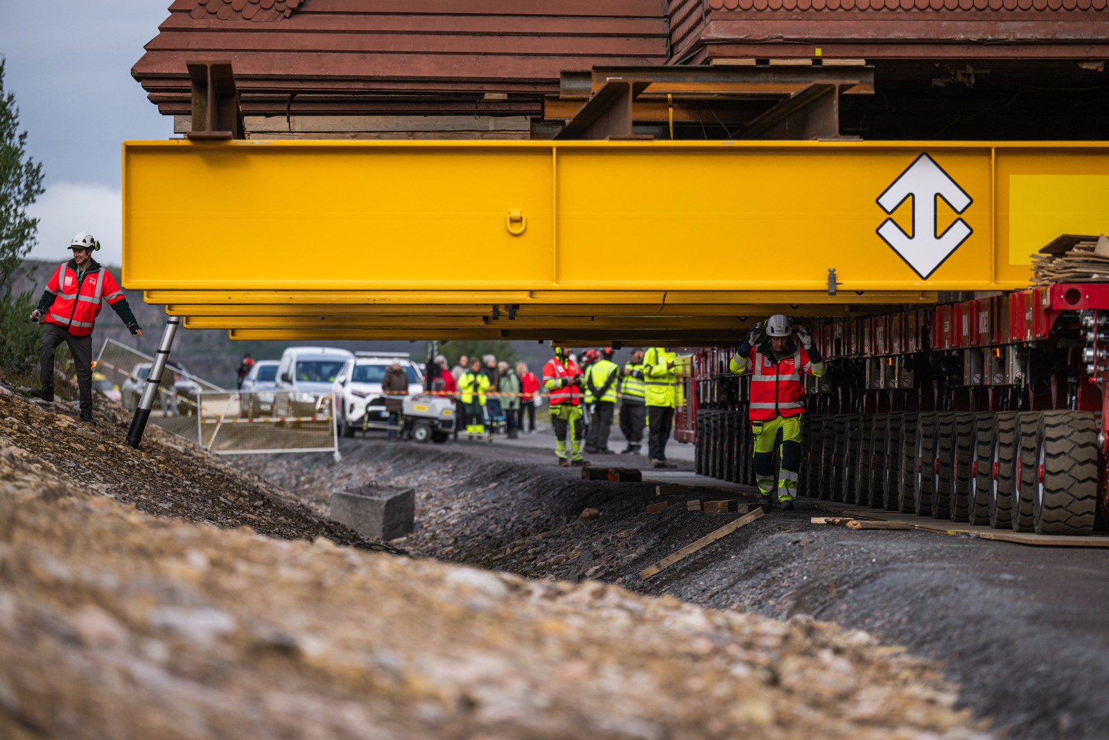 Workers walk along side and beneath beams supporting a church being rolled down a road