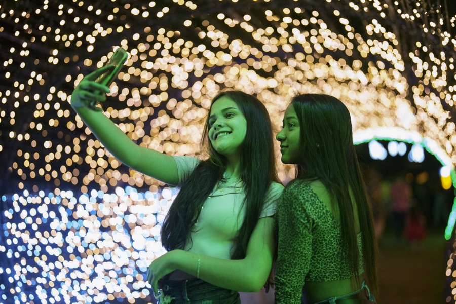 Two people take a selfie under an arch of Christmas lights.