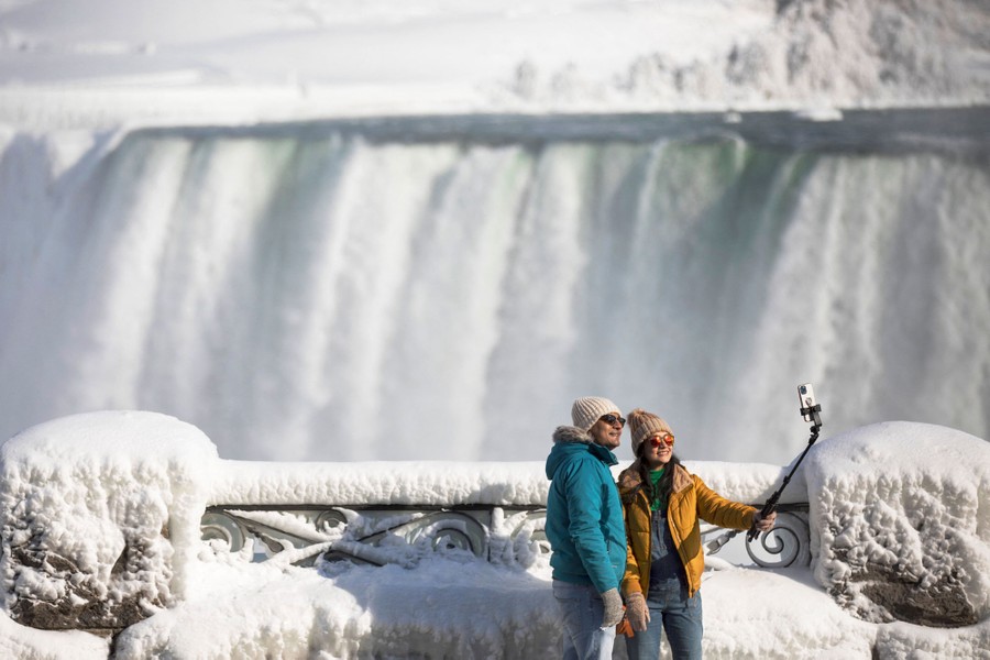 Tourists take a selfie overlooking Niagara Falls, among snow and ice.