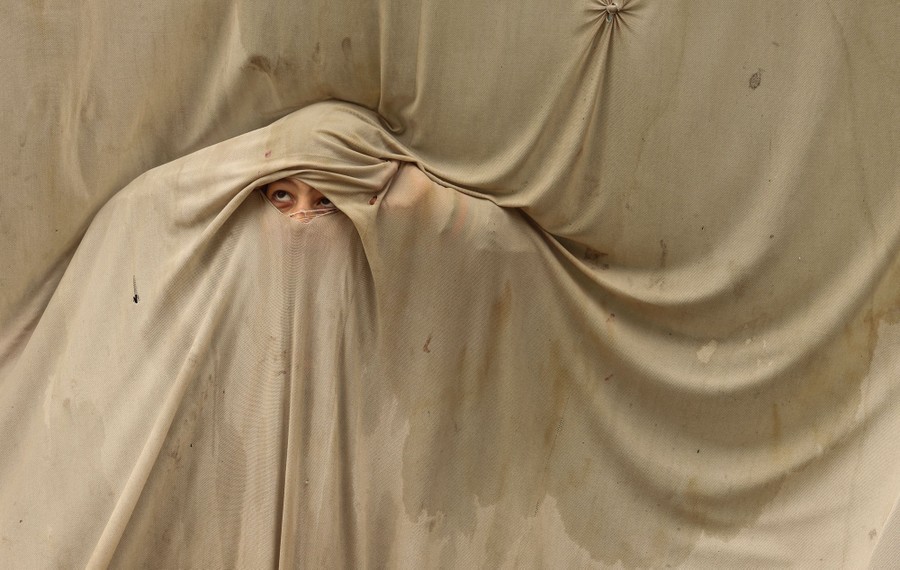 A young boy peeks out from a hole in a curtain.