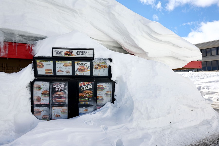 A Carl's Jr. drive-through menu is partially buried in a snowbank.