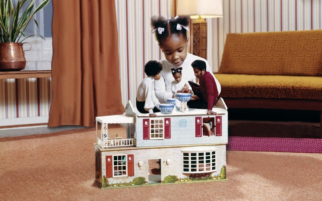 A young child plays with a doll version of her family in a dollhouse