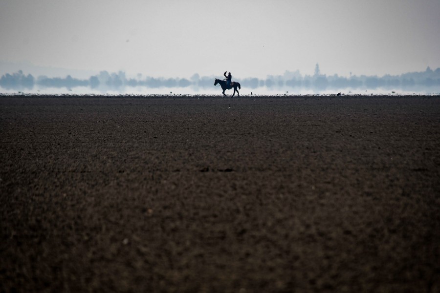 A single horse and rider are seen in the distance, riding across flat, dry land.